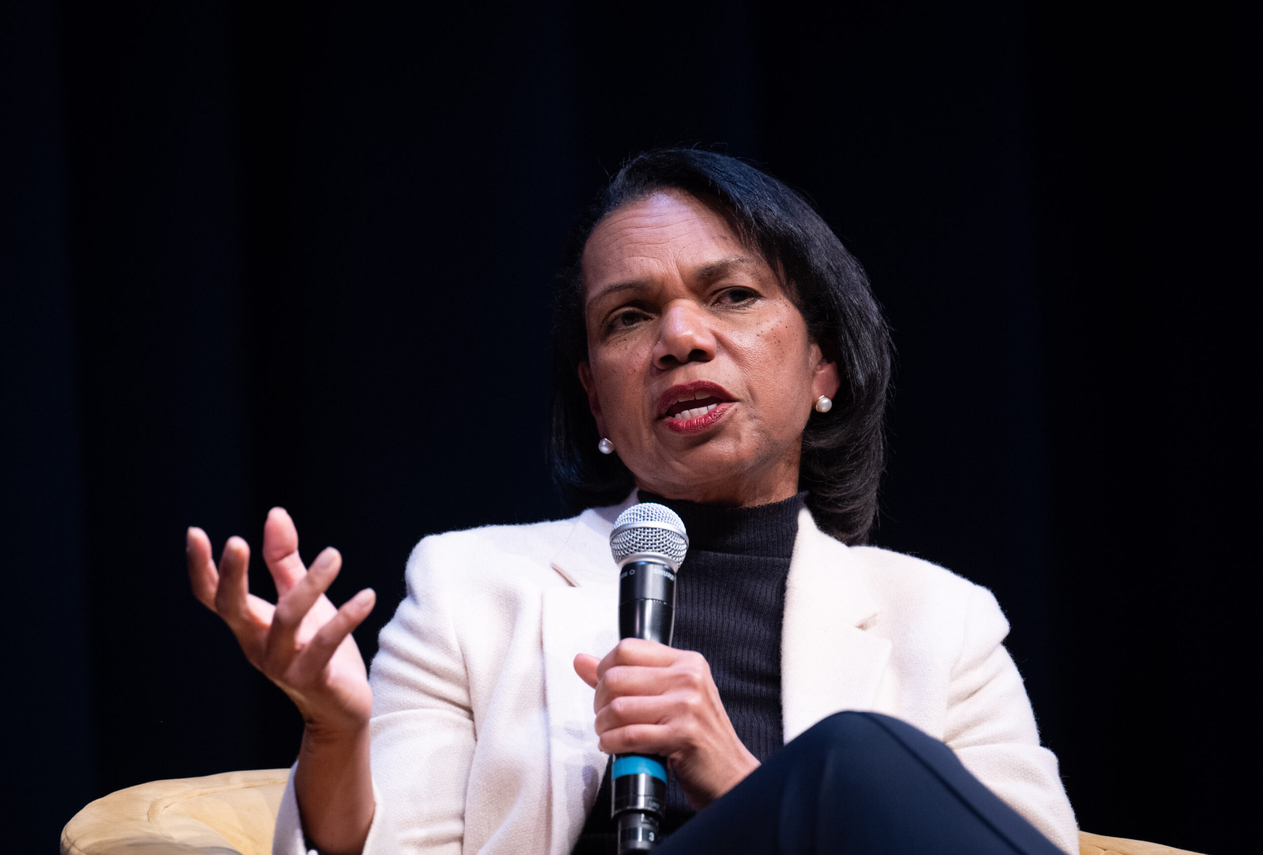 Condoleezza Rice speaks into a microphone while having a conversation with others on a stage.