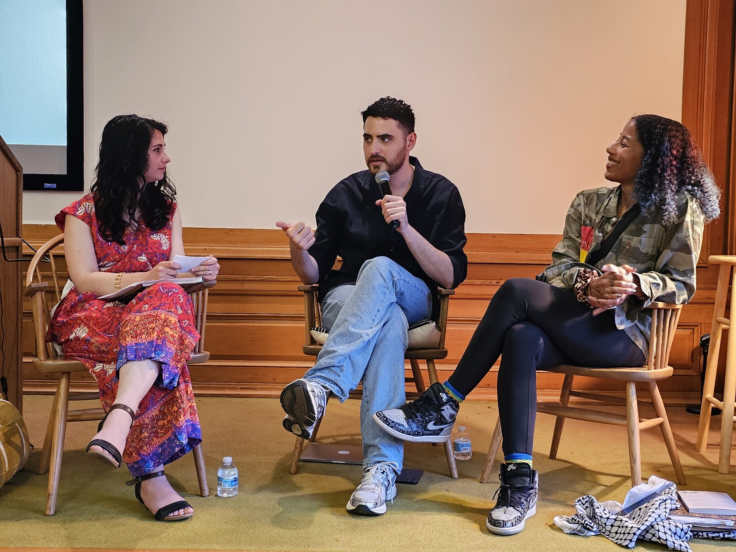 3 people sit in a group. The middle person speaks into a microphone while the other two listen intently.